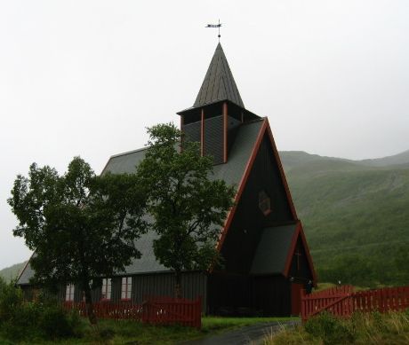 Arnøy kirke sett fra parkeringsplassen. Sommer, men bildet er preget av tåke.